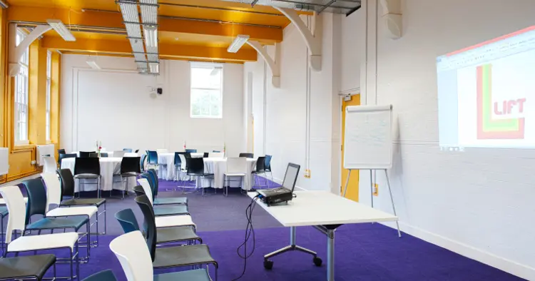 Penton room showing split set up half theatre style and half cabaret style and Lift logo projected onto wall