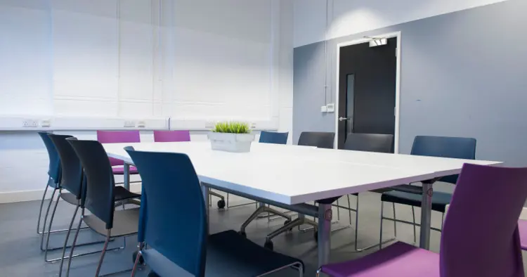 Board room set up for 12 people - white table, grey walls, purple and navy chairs