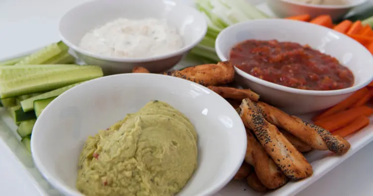 Dip bowls with guacamole, red salsa, cream cheese and hummus