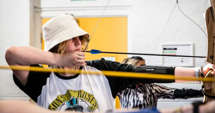 Young man wearing hat is drawing a bow