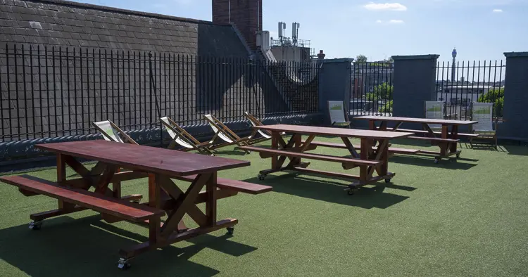 Roof terrace with green grass, four wooden tables and view to BT tower